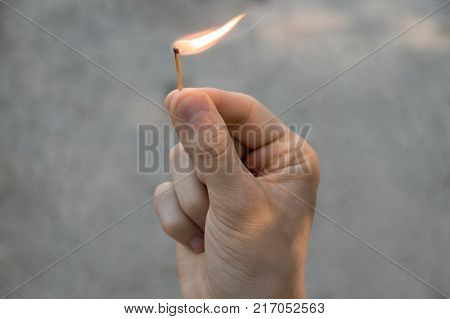 Right hand of adult man hold one match with sand background. The flame from the match pointing to the right.