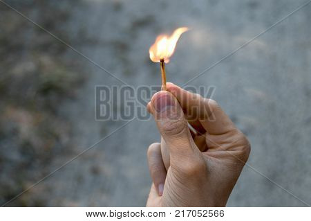 Right hand of adult man hold one match with sand background. The flame from the match pointing to the up and right.