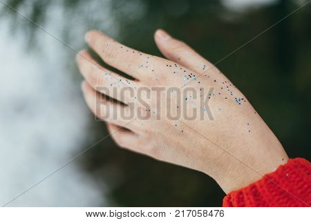 Young beautiful girl blowing on hands with blue glitters on green background.