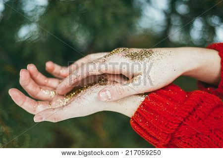Young curly girl in crystal sunglasses blowing on hands with golden glitters on blue background.