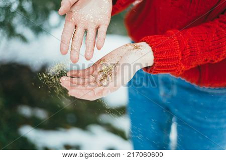 Young curly girl in crystal sunglasses blowing on hands with golden glitters on blue background.