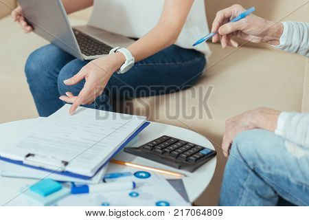Necessary document. Clever responsible financial advisor feeling confident while sitting on a sofa with a modern laptop on her knees and pointing to the necessary documents