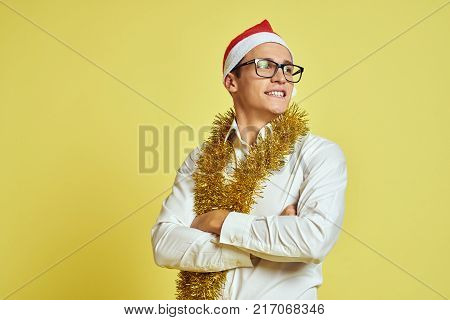 a man with glasses and a white shirt with tinsel on his neck crossed his arms over his chest, free space for copying, new year, holiday, light yellow background.
