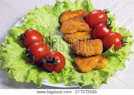 Close-up. Chicken nagets in breadcrumbs on green lettuce leaves with tomatoes in a white plate.