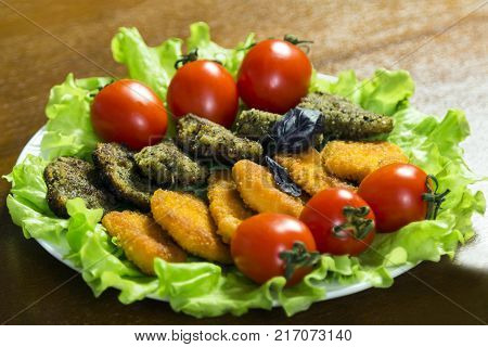 Close-up. Tasty meat or fish nagets in a plate on green lettuce leaves decorated with tomatoes.
