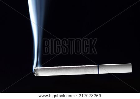 A white cigarette with a blue strip begins to burn and smoke on a dark background.