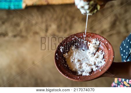 Close up hands holding bowl with copra and adding milk to it to cook dough
