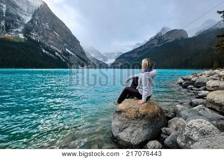 Woman sitting on rock in Lake Louise and enjoying the view of Victoria Glacier. Canadian Rockies. Banff National Park. Alberta. Canada.