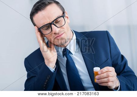 Terrible experience. Depressed exhausted young man touching his head with closed eyes while holding medication