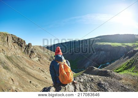 back view of woman traveler on a walk in the Valley of the river of Hveragerdi Iceland. Hiking Tour of Reykjadalur Hot Springs. woman sits on the cliff and looks at the sun