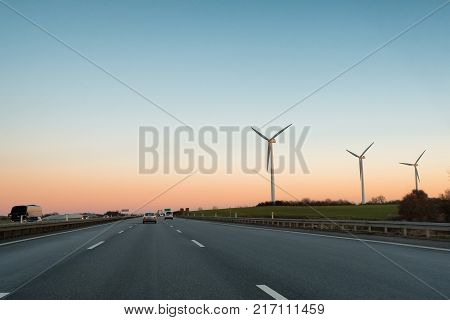 Multi-lane expressway at sunset. Highway. Three wind power plant generators are to the right of the road.