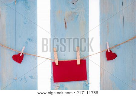 Red paper note and hearts on a string - Empty red message card surrounded by red hearts tied to a linen string with wooden clips on a blue fence.