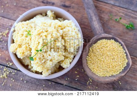 Raw millet on a wooden spoon and boiled millet in a bowl.