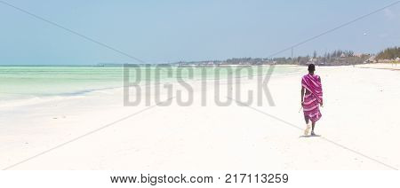 Unrecognizable Maasai warrior walking on picture perfect tropical sandy beach of Paje, on Zanzibar island, Tanzania, East Africa.