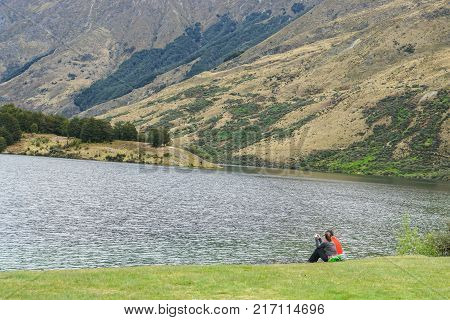 young couple sit on green yard at lake in mountain range for relaxation in holiday