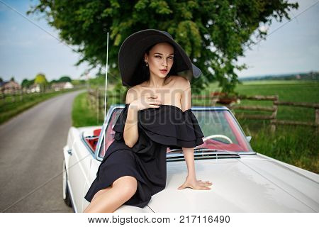 Beautiful young girl in a black hat driving vinage car