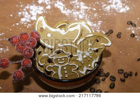 Christmas gingerbreads with white icing in a colorful bowl on a wooden board with flour and coffee beans for decoration