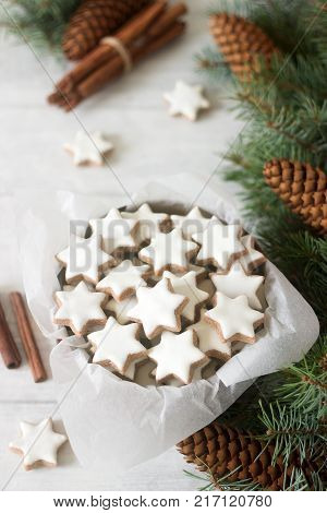 Cookies cinnamon star in a tin box on a background of cinnamon sticks, fir branches and cones. Selective focus.