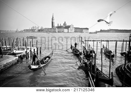 VENICE, ITALY - APRIL 11, 2017: Gondolas with tourists on background of San Giorgio Maggiore Monastery, black and white documentary snapshot. Venezia, Italy.