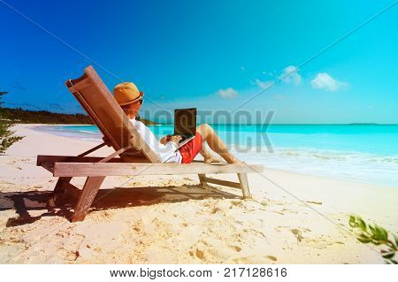 young man working on laptop at tropical beach, remote work concept