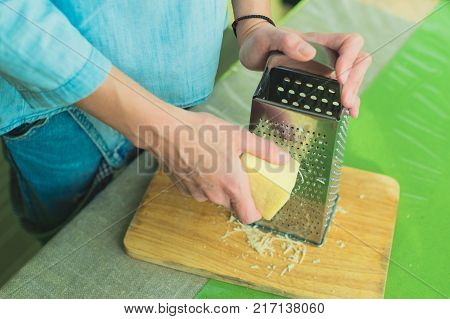 Close-up of a woman's hands rub a parmesan cheese on a metal grater on a green table