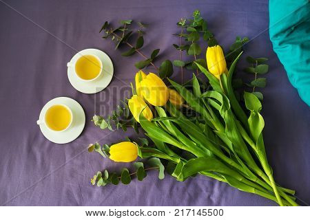 Yellow tulips and two cups of tea in bed, morning