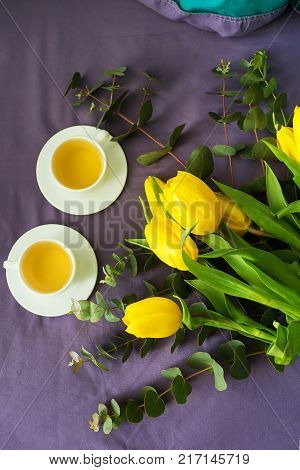 Yellow tulips and two cups of tea in bed, morning