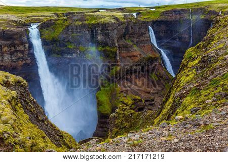 High waterfall Hayfoss in a picturesque and dangerous tundra canyon. Cloudy and windy summer day in Iceland. The concept of extreme and phototourism