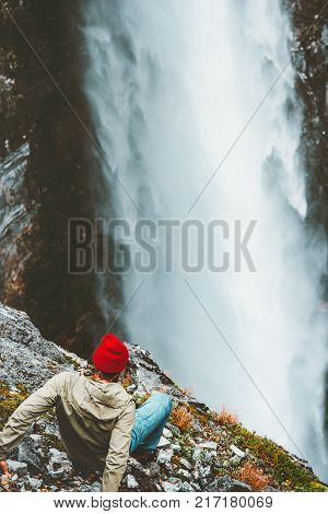 Man tourist on cliff looking at waterfall outdoor Travel Lifestyle success concept adventure vacations in mountains