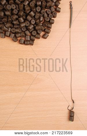Fishing bait with hook and brown pre-drilled halibut pellets for carp fishing isolated on wood background with soft shadow