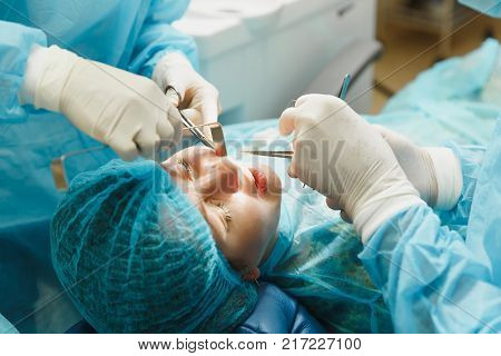 Male Old Professional Dentist Surgeon In Uniform And Female Assistant Helps To Performing Operation