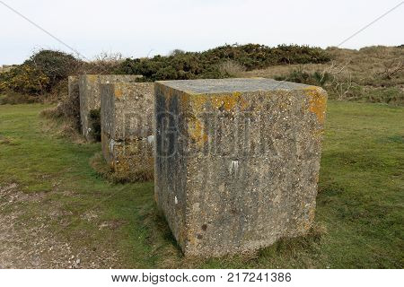 Line of World War Two concrete block tank traps on the edge of a beach on the east anglian coast of the U.K. Background of sand dunes with gorse and a grey sky.