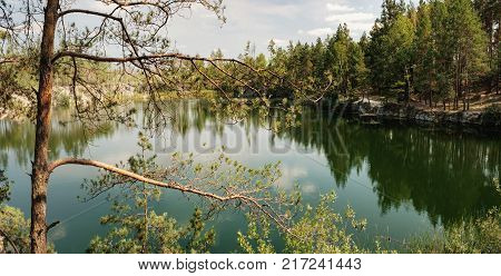 Picturesque landscape with a lake in the middle of a coniferous forest in Korostyshiv quarry, Zhytomyr district, northern Ukraine. Branches of pine overhanging lake in the foreground