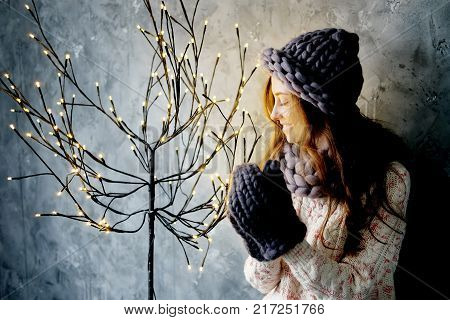 Winter fashion accessories.Young woman dressed for cold weather in grey snood hat and mittens admiring christmas lights.