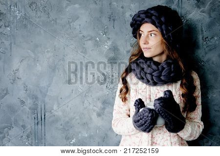 Winter fashion accessories.Young woman dressed for cold weather in grey snood hat and mittens holding a cup of tea.