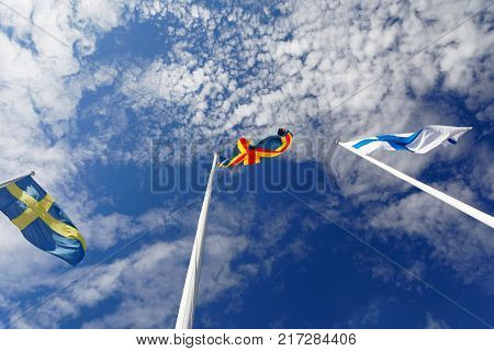 Flags from Sweden Aland and Finland on flag poles blue sky and white cloudes