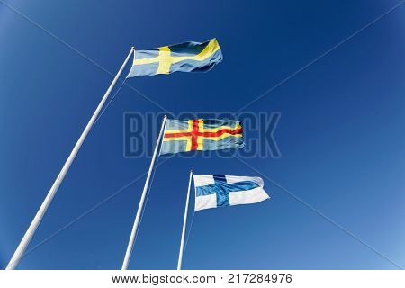 Flags from Sweden Aland and Finland on flag poles blue sky and white cloudes