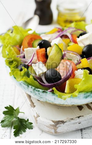 Greek salad in a ceramic plate on a white wooden background. Traditional Greek dish. Selective focus.Top view.