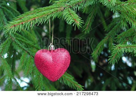 The decoration on the Christmas tree. Red heart hanging on a Christmas tree. Christmas tree. The spirit of Christmas. Christmas traditions. Winter mood and love. Heart on the snow. Valentines Day