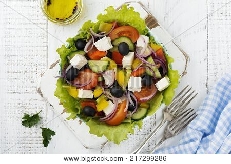Greek salad in a ceramic plate on a white wooden background. Traditional Greek dish. Selective focus.Top view.