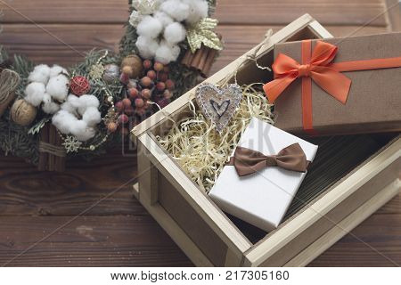 A New Year surprise in a wooden box. A white gift box with a brown sation bow and a brown gift box with an orange ribbon. A pine wreath with natural decorations. Rustic wooden background