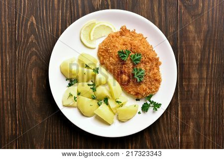 Schnitzel with boiled potato on plate over wooden background. Top view flat lay food