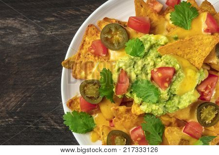 An overhead closep photo of nachos with queso, traditional Mexican snack, on a rustic background with a place for text