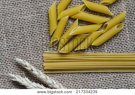 Still life for a kitchen of wheat ears and pasta from wheat on a sackcloth background.