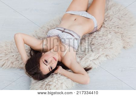Pretty sexy young woman laying on the floor in a gray lace underwear on the white background. Close up of lady. Beauty concept.