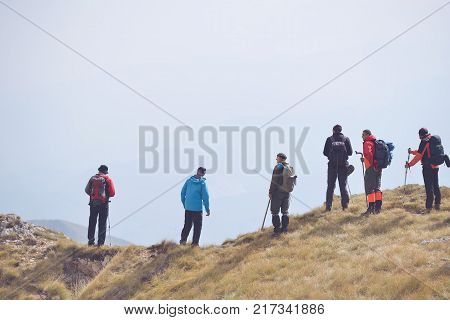 Group of People of different age and ethnicity walking up on Mountain Trail during Hike carrying heavy backpacks and climbing gear led by mature Guide.