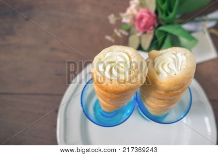 Two cream horns pastry horn with white cream filling creamy cones in the blue glass on wooden table background.