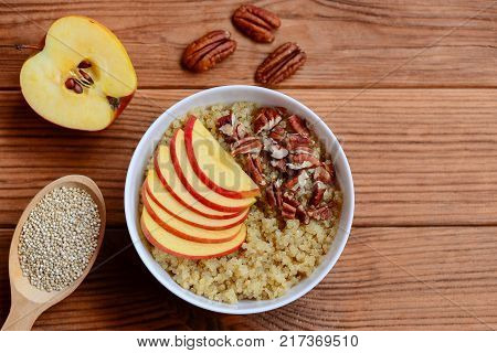 Quinoa porridge with mixed topping. Easy Breakfast quinoa porridge with fresh apples and pecan nuts in a white bowl and on brown wooden background with empty space for text. Quick sweet dish. Top view