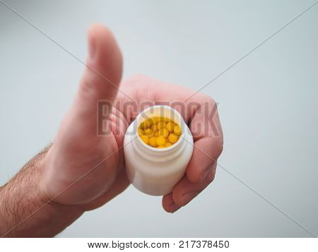 Yellow balls background. Vitamins in a hand on a white background. Against a background of pusyrek with vitamins. Thumbs up.