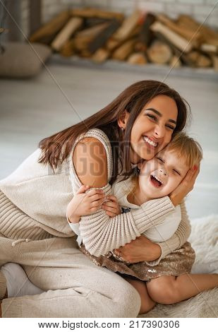Mother sits on floor and embraces her little daughter and they are laughing cheerfully.